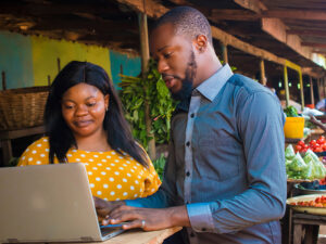A man and a woman working in partnership at a laptop together in a rural food market